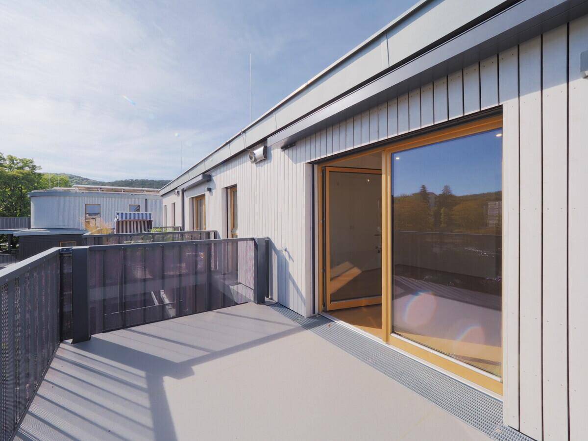 Geräumiger Balkon mit Holzelementen an der Fassade und Zugang zu einem hellen Innenraum.