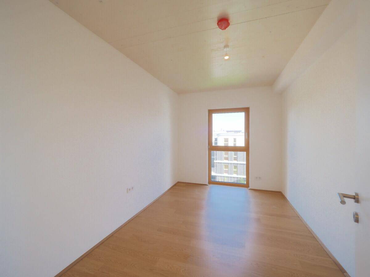 Geräumiges Schlafzimmer mit hellem Parkettboden und einem großen Fenster für optimale Belichtung.