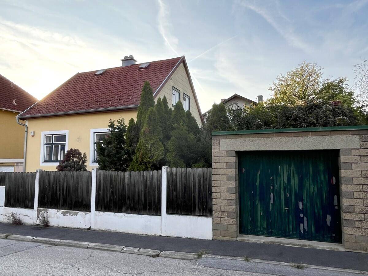 Ansicht des Hauses von der Straße mit angrenzender Garage und Holzzaun.