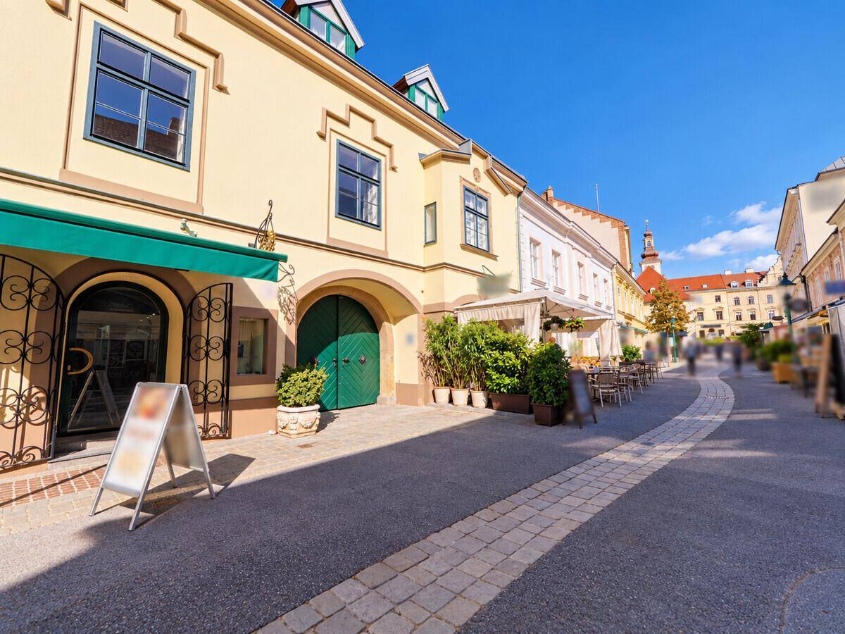 Malerische Straße mit historischen Gebäuden, Außengastronomie und blauem Himmel.
