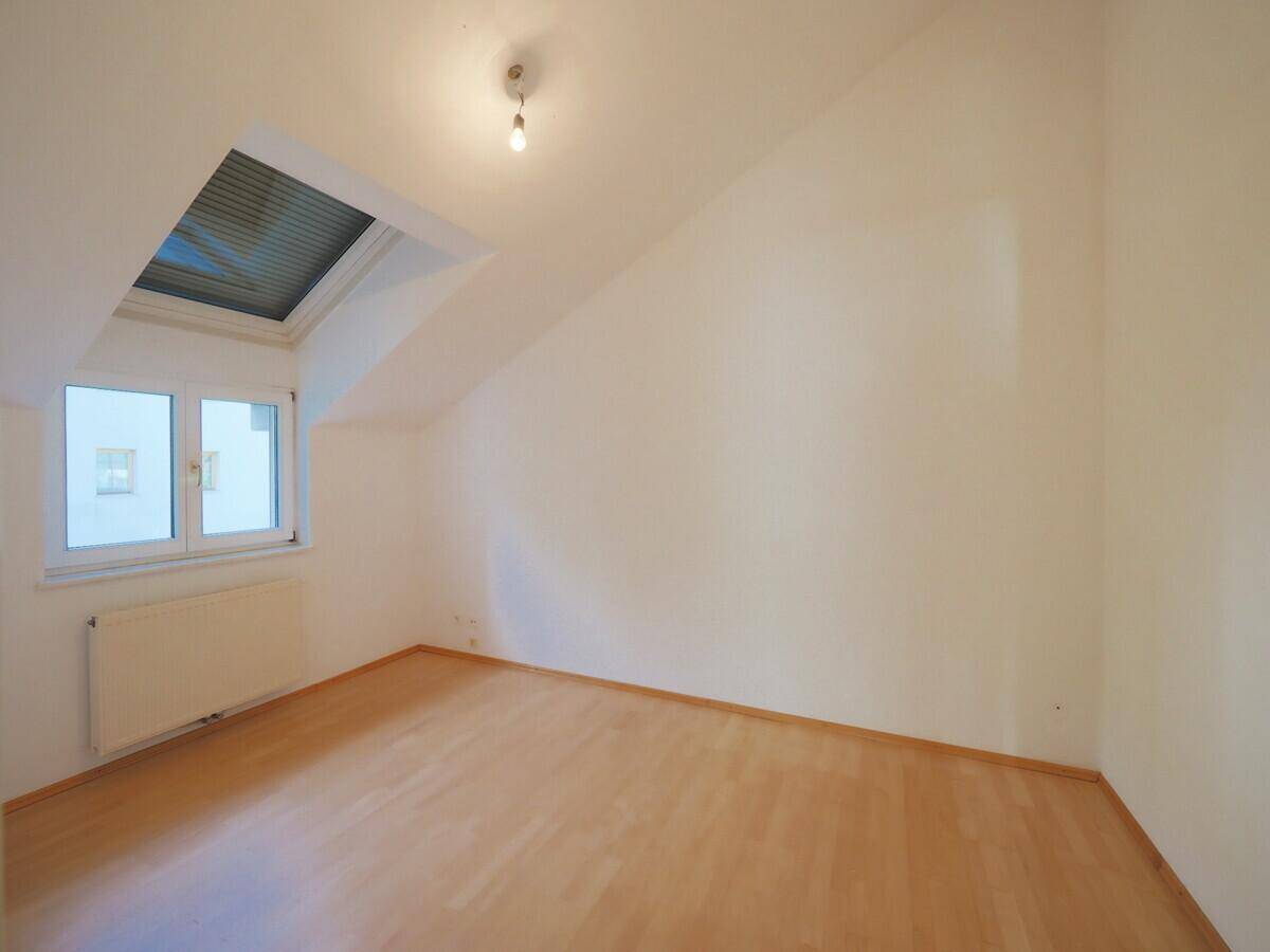 Helles Zimmer mit Holzboden, Dachschrägen, Fenster und einem zusätzlichen Dachfenster für viel Licht.