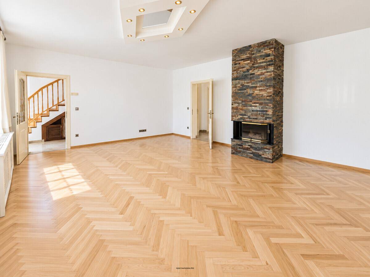 Geräumiges Wohnzimmer mit Kamin, Fischgrätparkett und indirekter Deckenbeleuchtung.