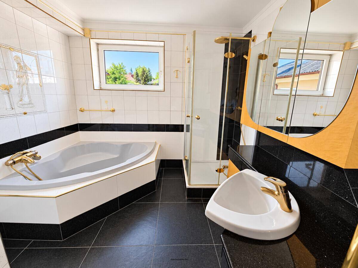 Badezimmer mit schwarzem Fliesenboden, Eckbadewanne, Dusche und goldenen Armaturen.