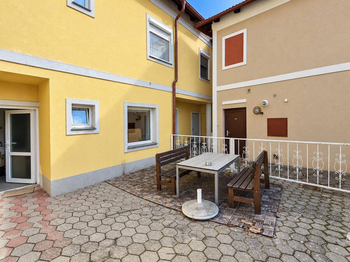 Gepflasterte Terrasse mit Sitzgelegenheiten zwischen zwei Gebäudeteilen.