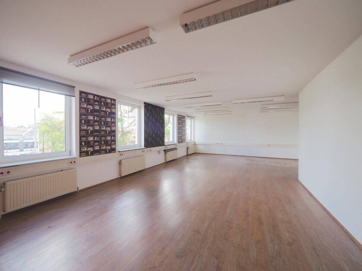 Großer Büroraum mit Laminatboden, vielen Fenstern und heller Beleuchtung.