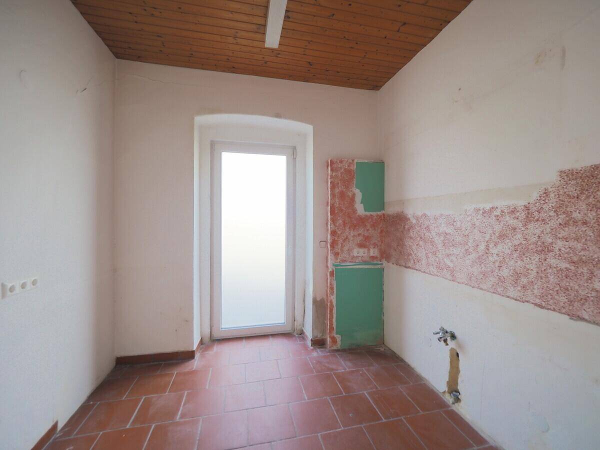 Küche mit Terrakottafliesen, Holzdecke und einem Fenster, renovierungsbedürftig.