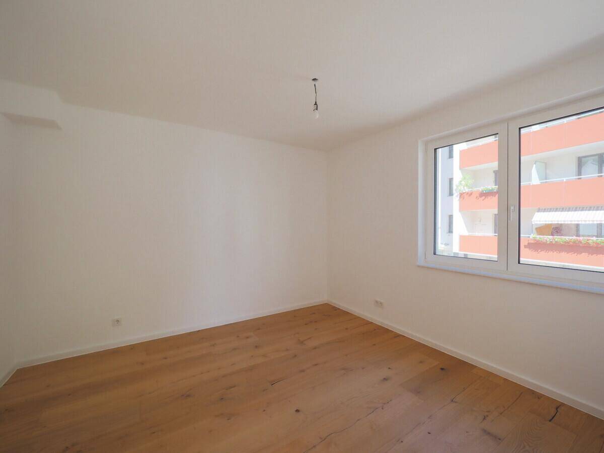 Helles Schlafzimmer mit Eichenparkett und großem Fenster mit Blick auf die Umgebung.