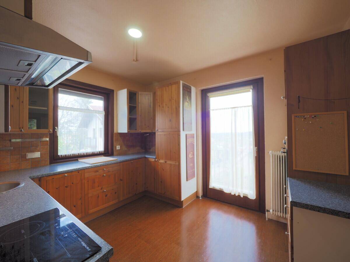 Funktionale Küche mit Holzschränken, dunkler Arbeitsplatte und Zugang zu einem Außenbereich.