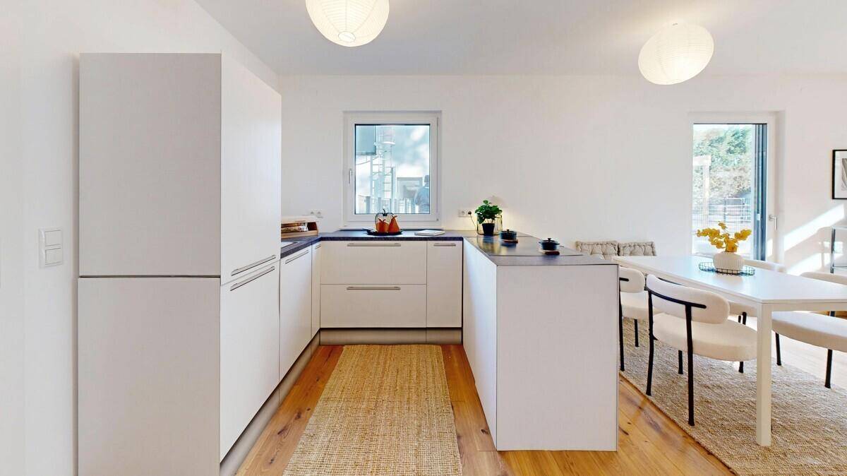 Moderne Einbauküche mit weißen Fronten, dunkler Arbeitsplatte und integriertem Essbereich.