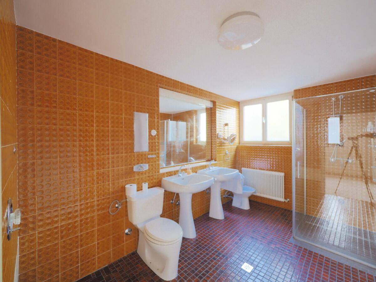 Geräumiges Badezimmer mit doppelten Waschbecken, Dusche und auffälligen orangefarbenen Fliesen im 80er-Jahre-Stil.