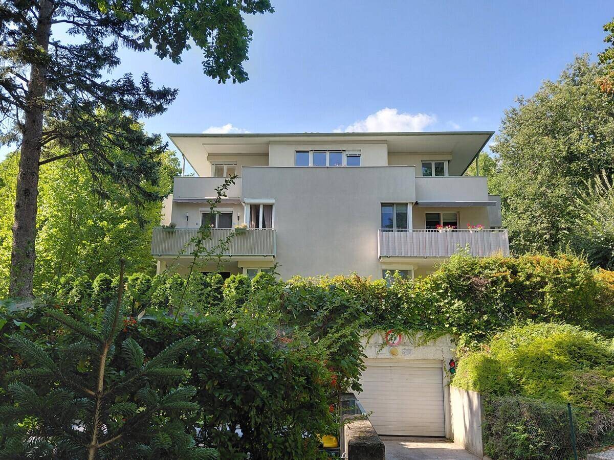 Moderne Wohnanlage umgeben von üppigem Grün, mit Balkonen und Tiefgaragenzufahrt.