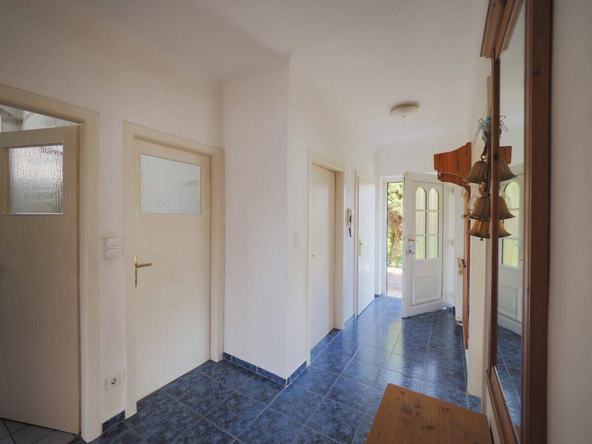 Heller Flur mit blauen Fliesen, mehreren Türen und einem Spiegel an der Wand.