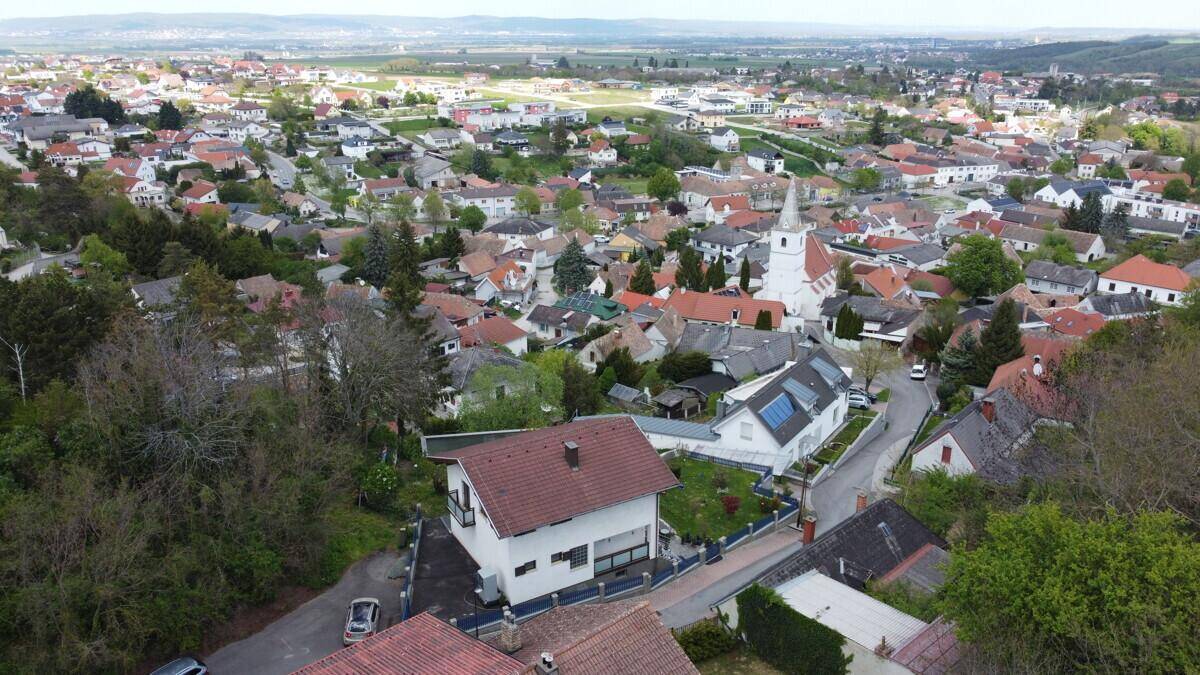 Luftaufnahme des Hauses mit Satteldach, umgeben von Bäumen und einer Wohnsiedlung.
