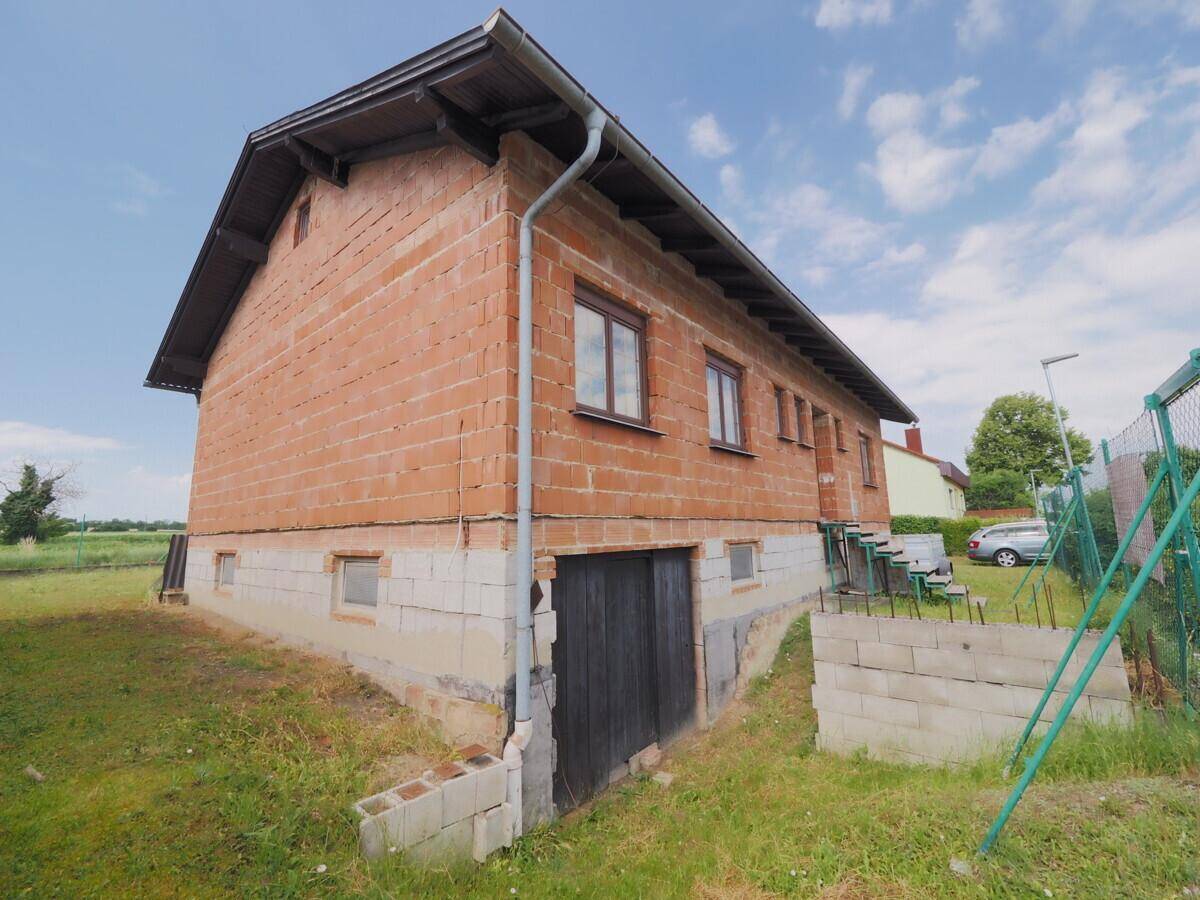 Rückseite des Hauses mit Kellerzugang und unverputzten Ziegelwänden im Rohbauzustand.