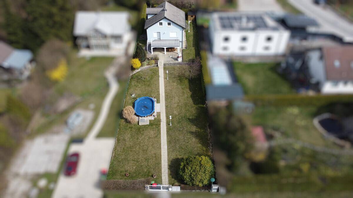 Luftaufnahme des Einfamilienhauses mit langem Garten und oberirdischem Pool.