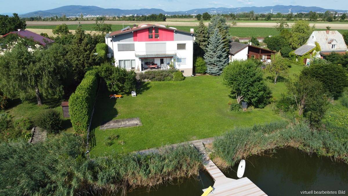 Luftaufnahme des Hauses mit großem Rasenbereich, umgeben von Bäumen und direkt am See gelegen.