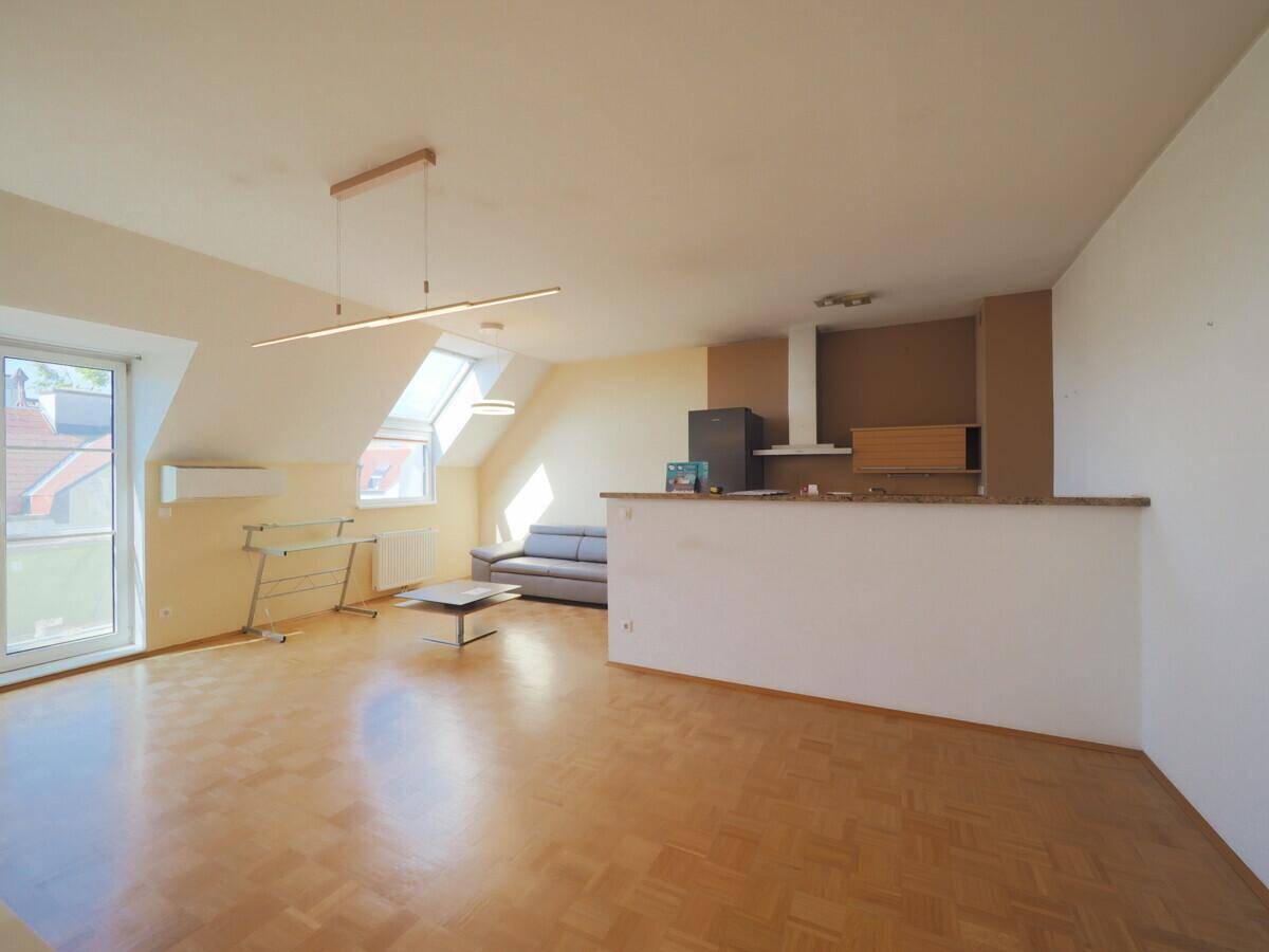 Offener Wohnbereich mit Parkettboden, Dachschrägen und viel Tageslicht durch große Fenster.