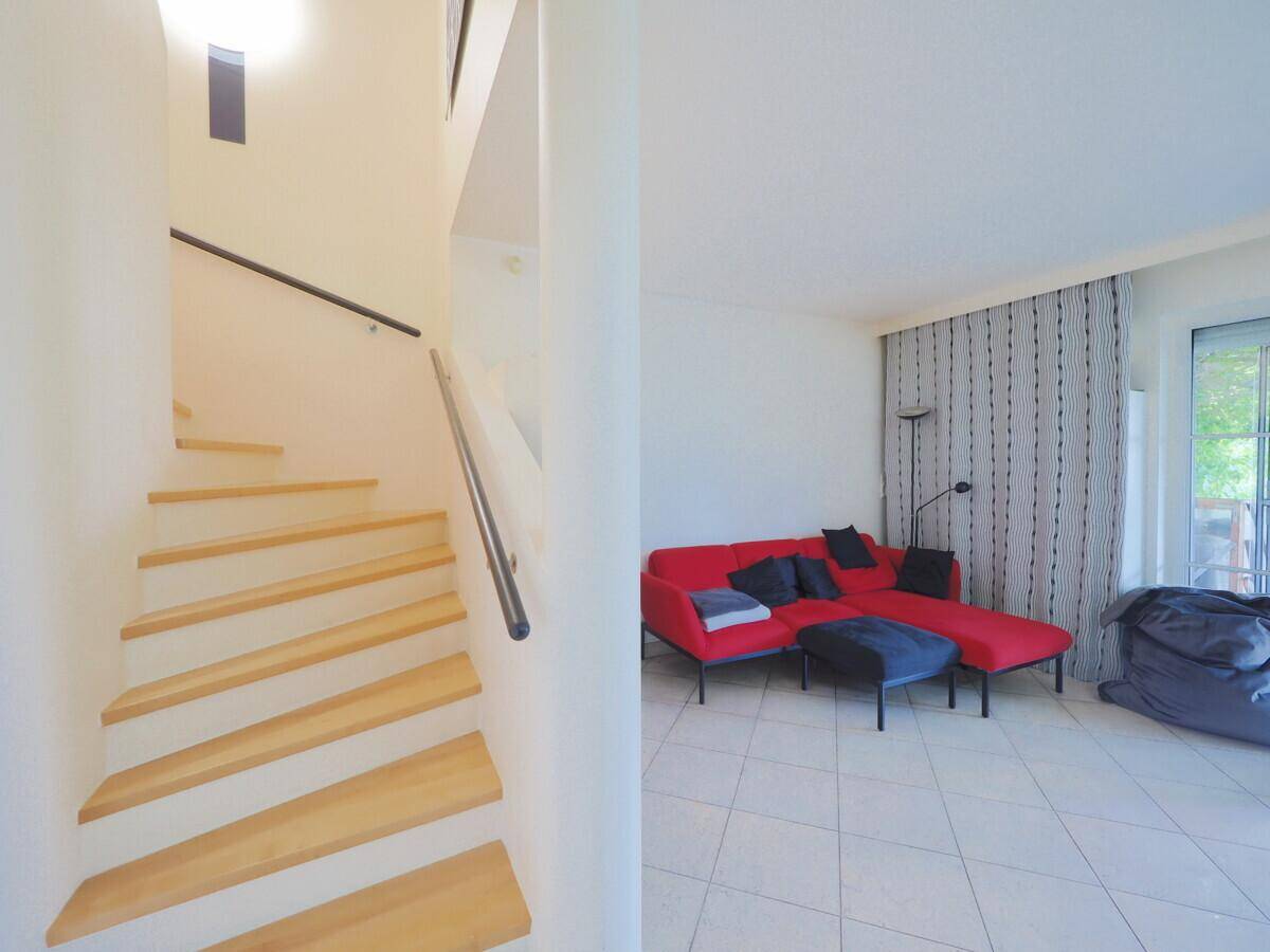 Heller Wohnbereich mit rotem Sofa und Holztreppe zum Obergeschoss.