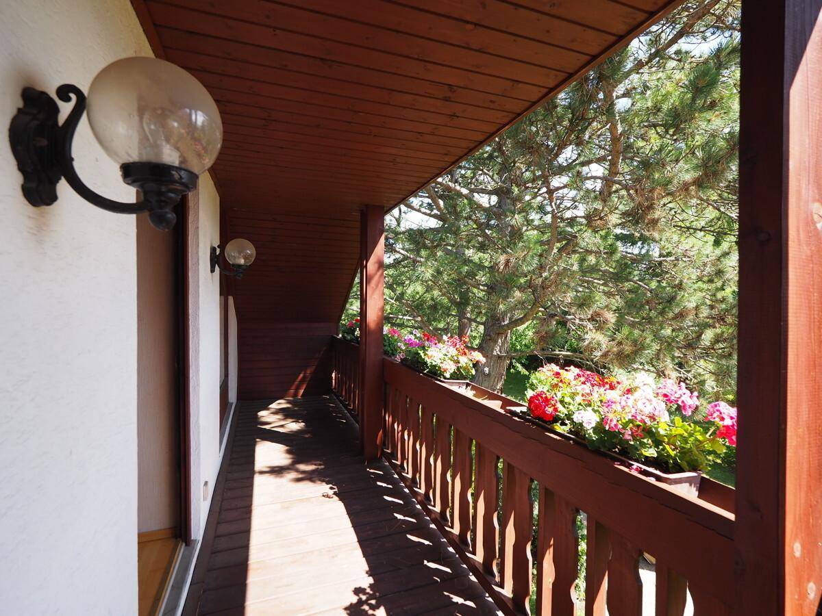 Langer Balkon mit Holzgeländer, Blumenkästen und Blick ins Grüne.
