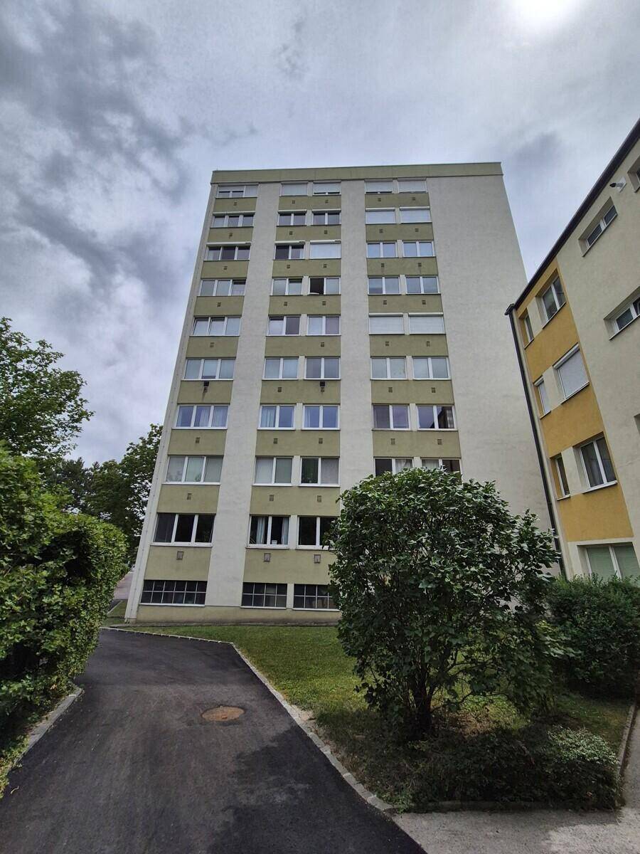 Hohes Mehrfamilienhaus mit vielen Fenstern und gepflegter Grünanlage im Außenbereich.