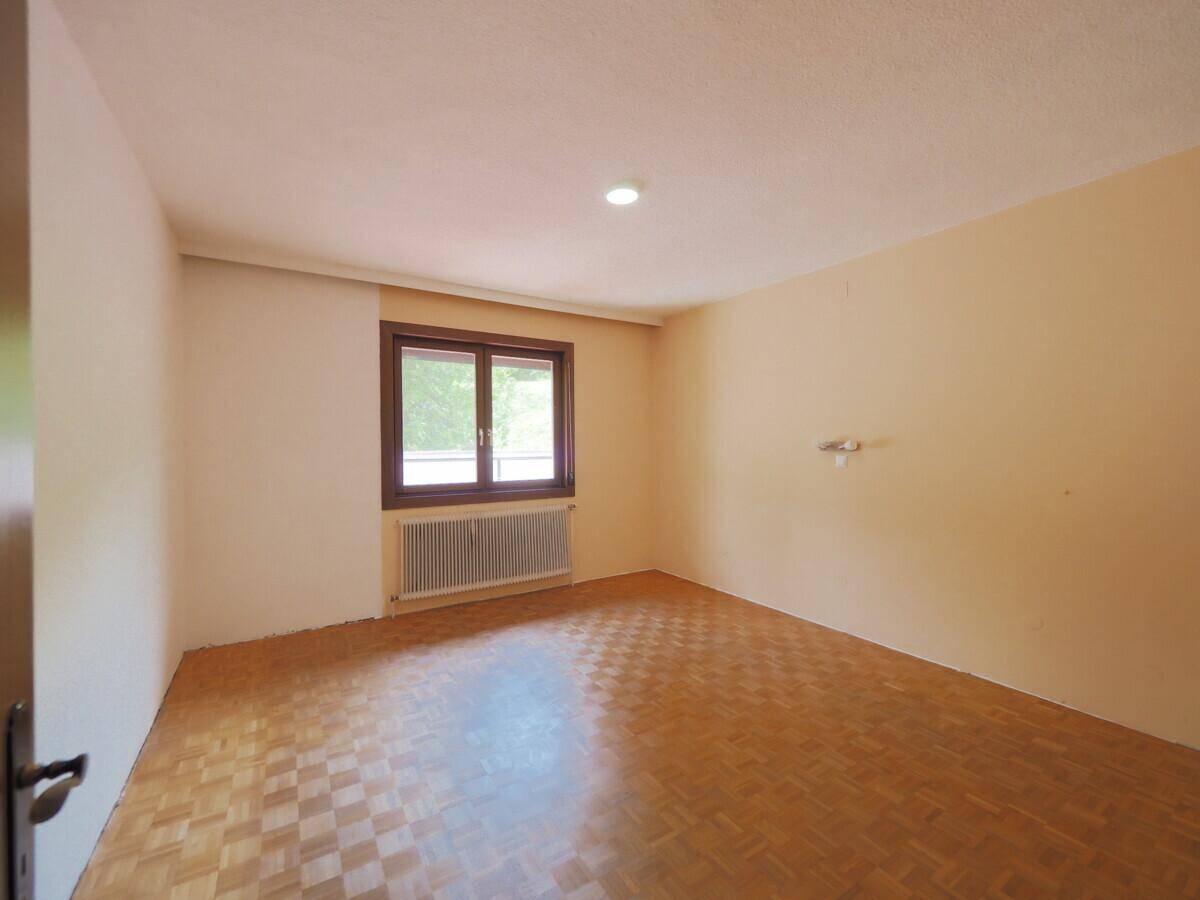 Leeres Schlafzimmer mit Parkettboden und einem Fenster, das viel Tageslicht hereinlässt.