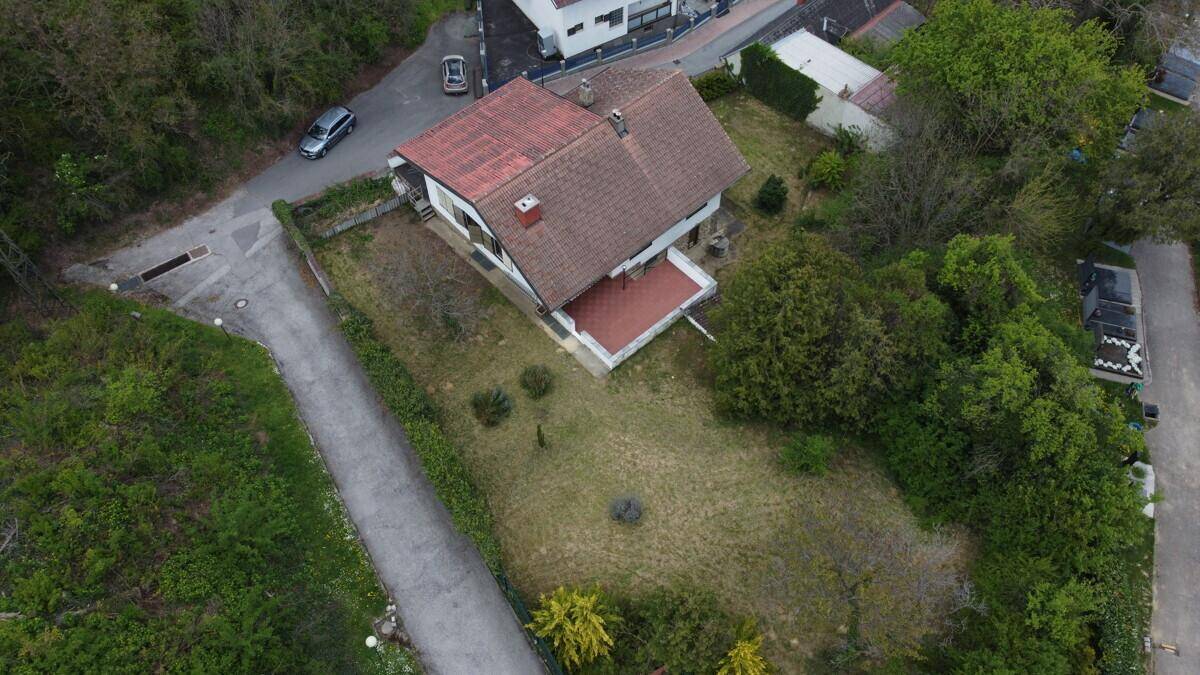 Luftaufnahme des Hauses mit rotem Ziegeldach, großem Garten und angrenzender Straße.