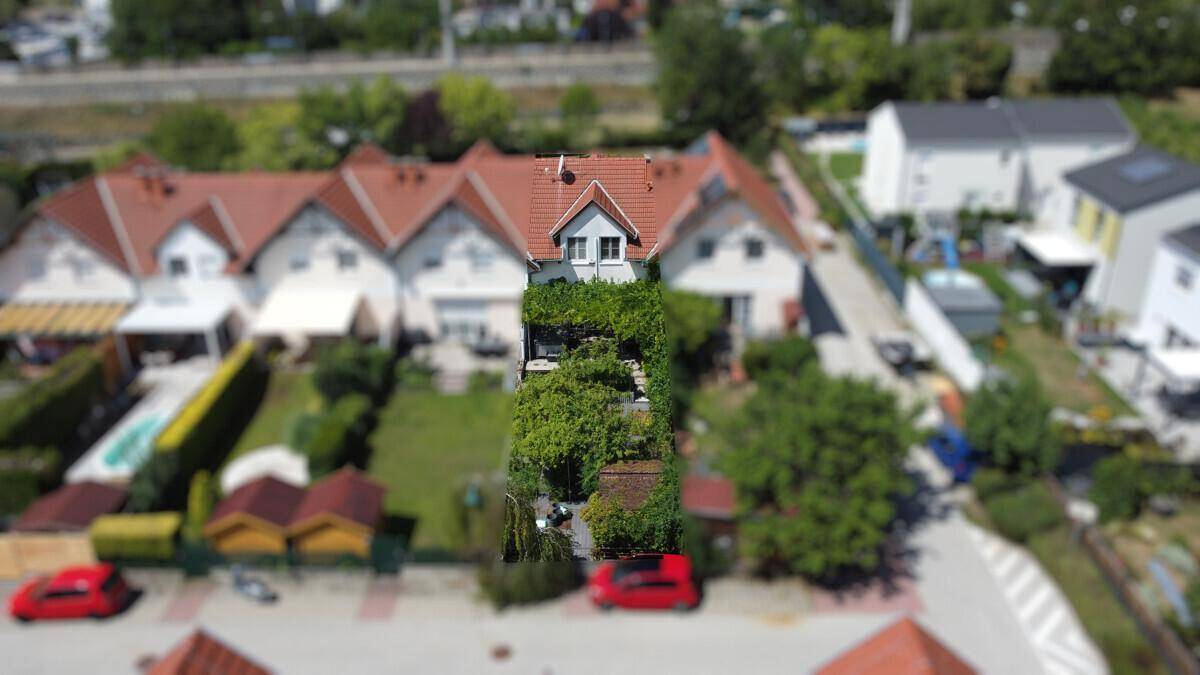 Luftaufnahme einer Reihenhaussiedlung mit grünen Gärten und roten Dächern.