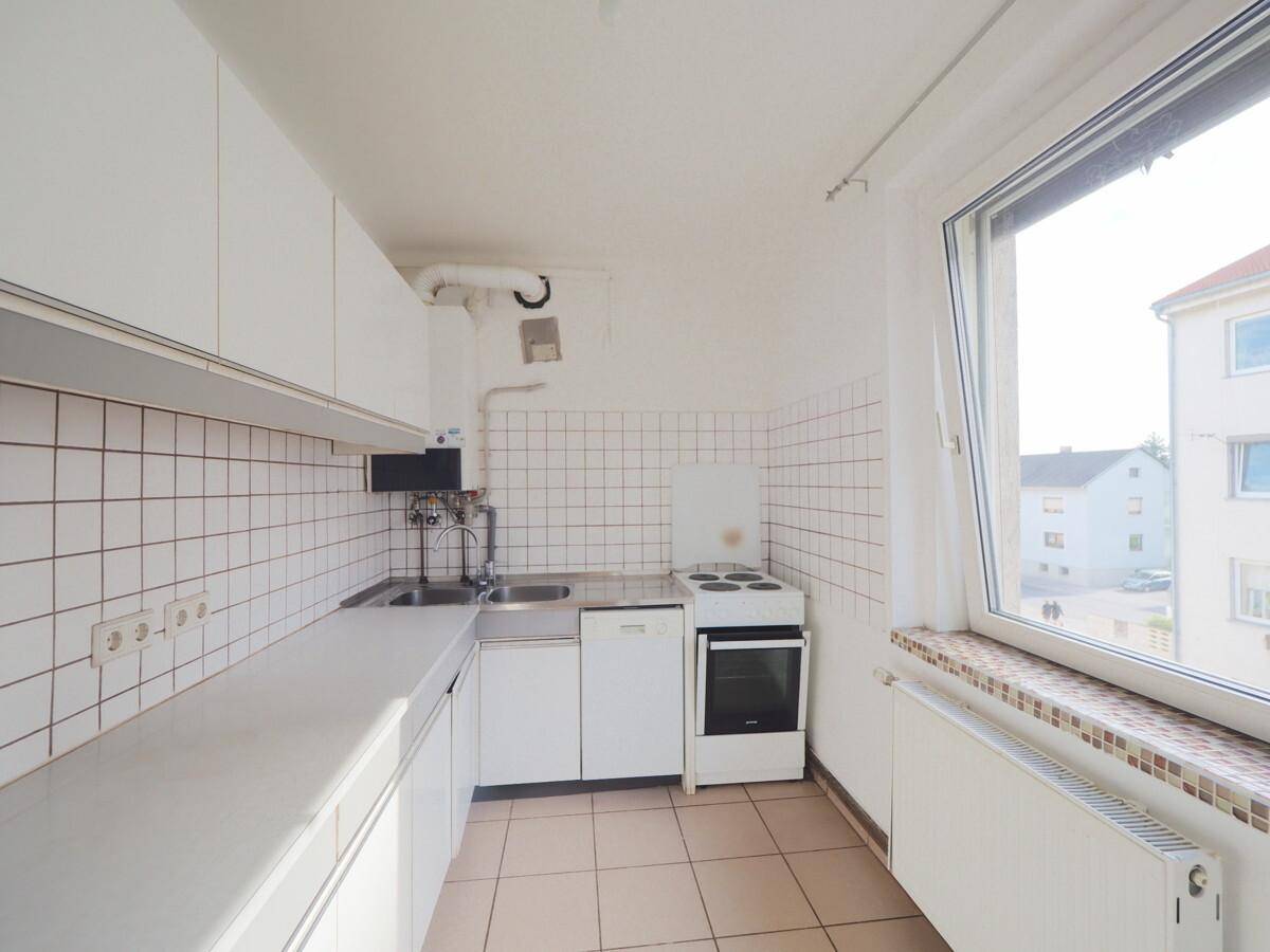 Kleine Küche mit weißen Schränken, Fliesenrückwand und Blick aus dem Fenster auf die Umgebung.