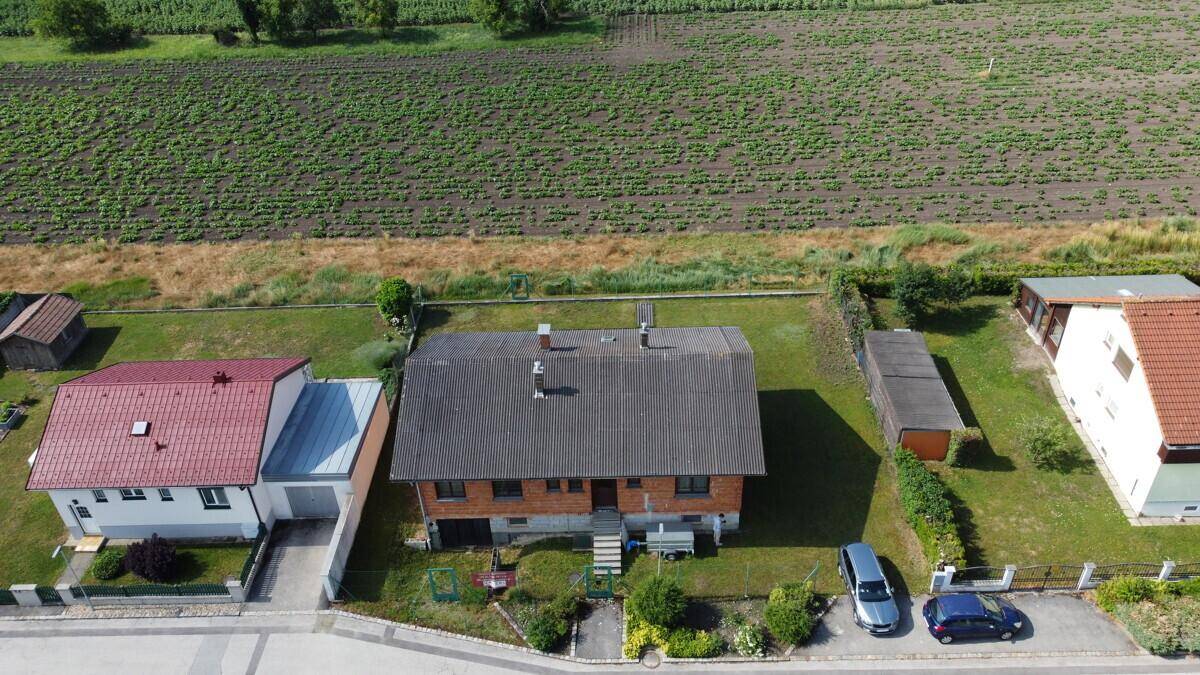 Luftaufnahme des Einfamilienhauses mit angrenzenden Feldern und Gärten sowie Parkplätzen.