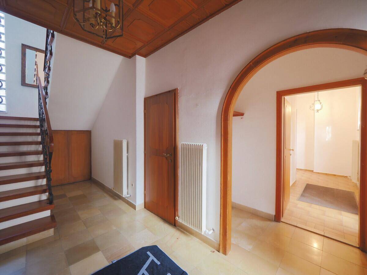 Eingangsbereich mit gefliestem Boden, Holztreppe und dekorativer Holzdecke, die zum Obergeschoss führt.