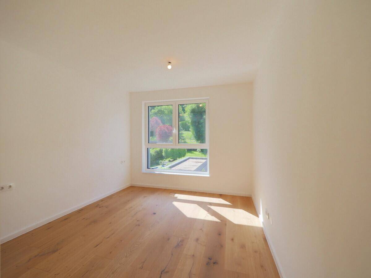Helles Schlafzimmer mit Holzfußboden, weißen Wänden und Blick ins Grüne.