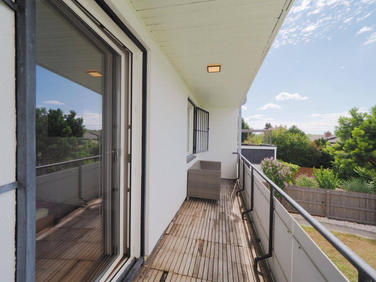 Balkon mit Holzbelag, Glasschiebetür und Blick ins Grüne.