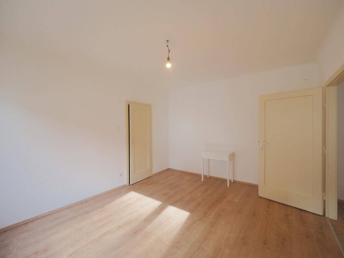 Leerer Raum mit Laminatboden, weißen Wänden und natürlichem Lichteinfall durch ein nicht sichtbares Fenster.