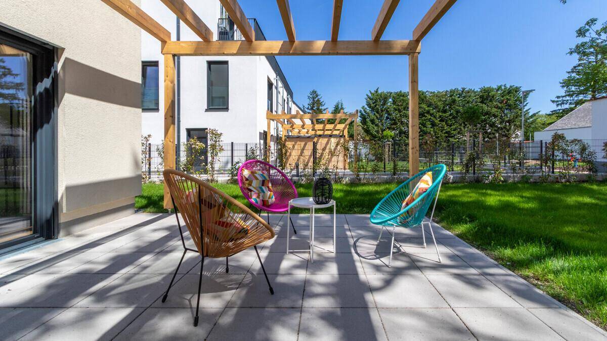 Helle Terrasse mit Holzpergola, bunten Sitzmöbeln und Blick auf die umliegende Grünfläche.