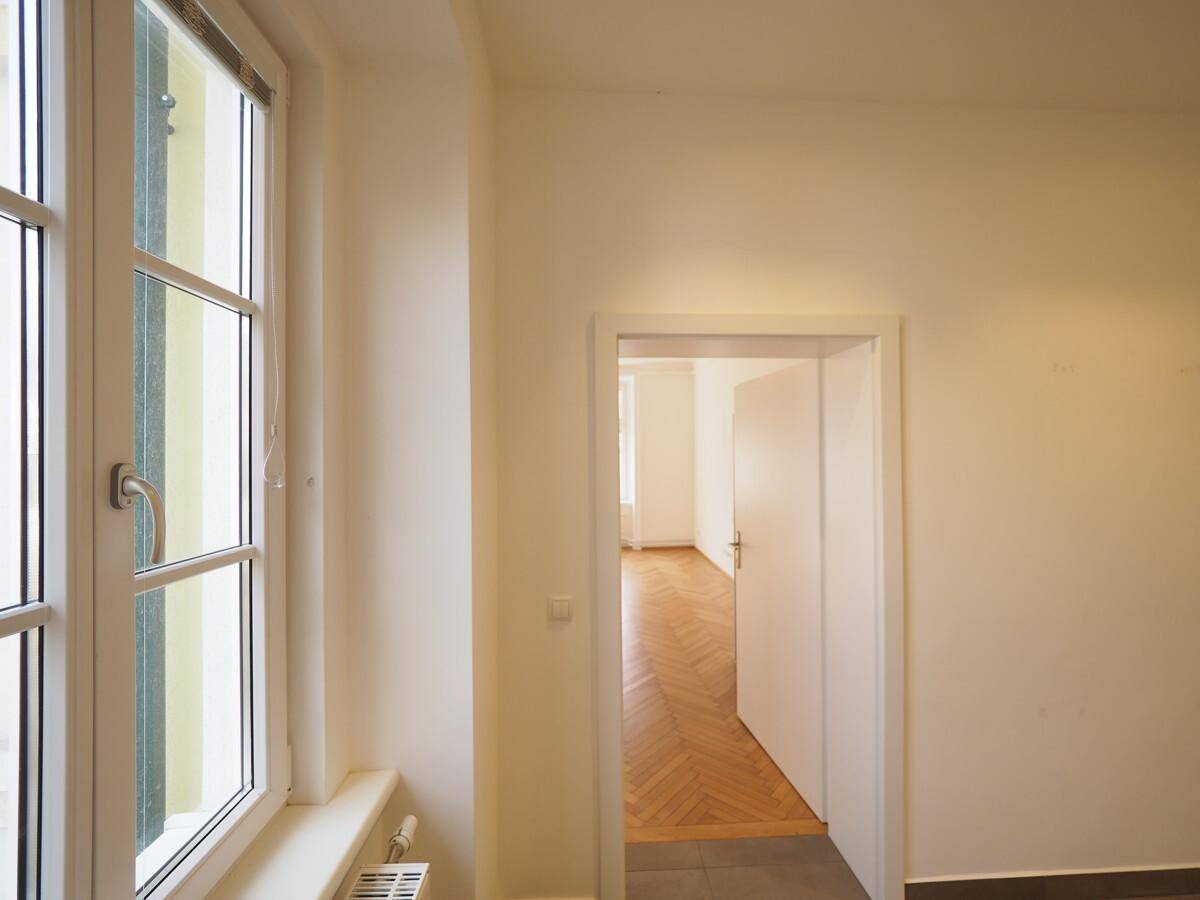 Heller Flur mit Fenster und Blick in einen weiteren Raum mit Parkettboden.