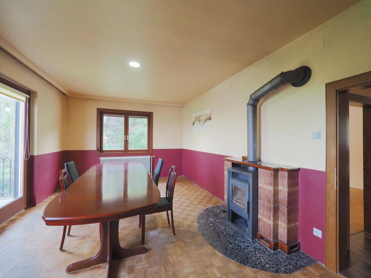 Geräumiges Esszimmer mit großem Holztisch, Kaminofen und Parkettboden, ideal für Familienessen.
