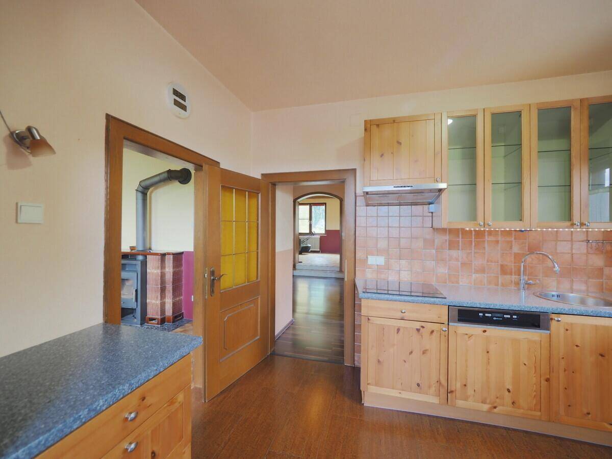 Gemütliche Küche mit Holzfronten, Fliesenrückwand und Blick auf einen Kaminofen im Nebenraum.