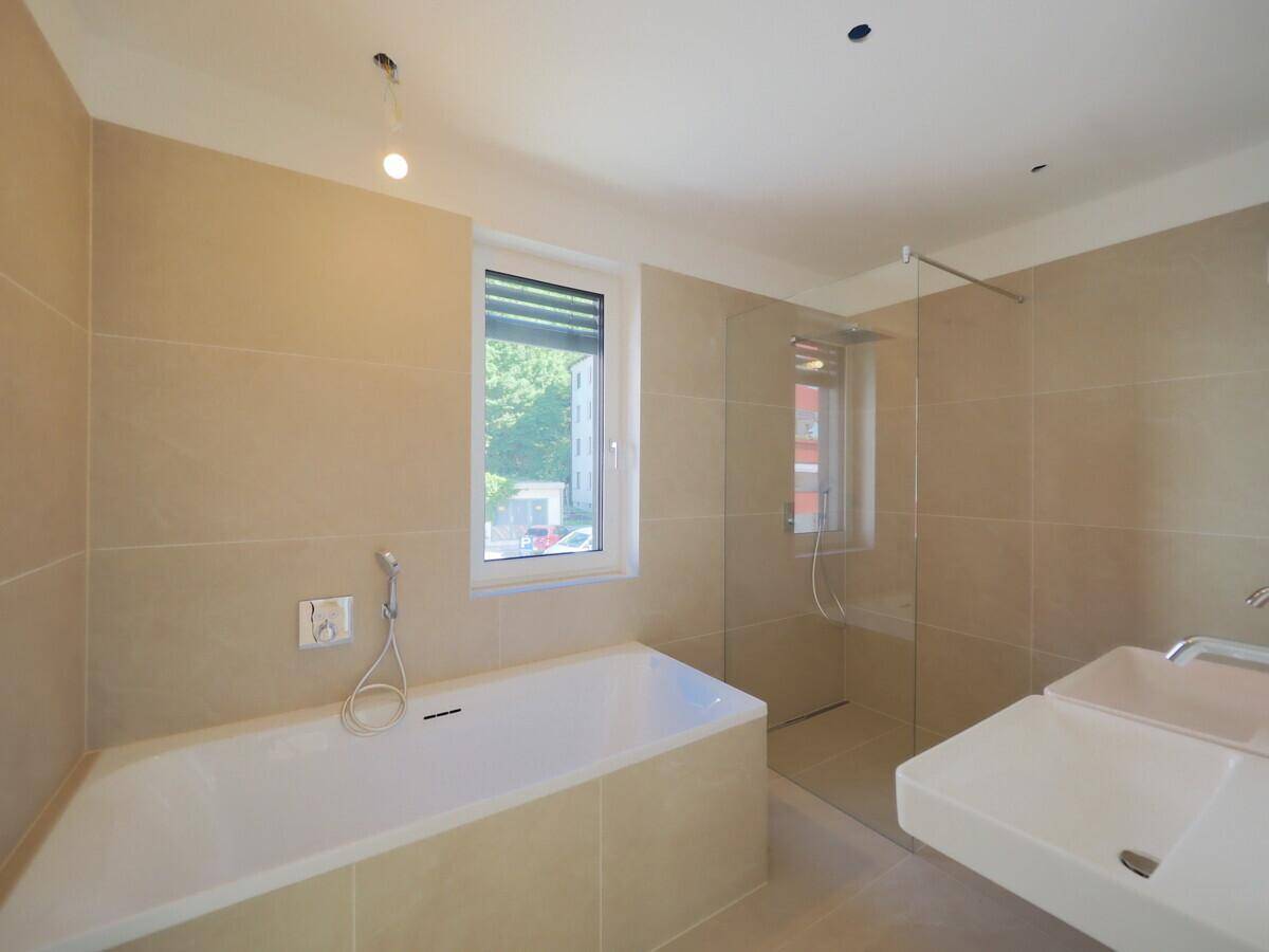 Modernes Badezimmer mit beigefarbenen Fliesen, Badewanne, ebenerdiger Dusche und Fenster.