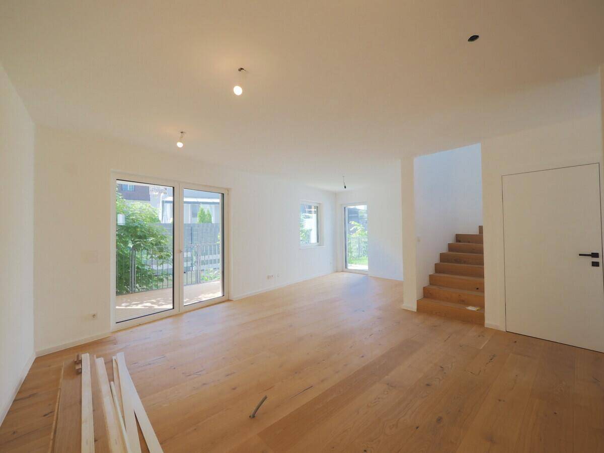 Helles Wohnzimmer mit Holzparkett, weißen Wänden und Zugang zu einer Außenterrasse.