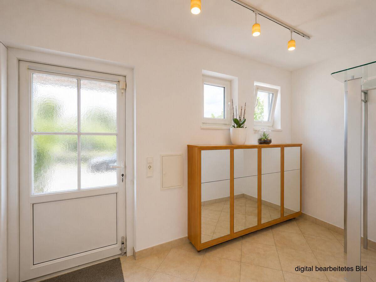 Eingangsbereich mit heller Tür, kleinen Fenstern und einem Spiegelschrank.