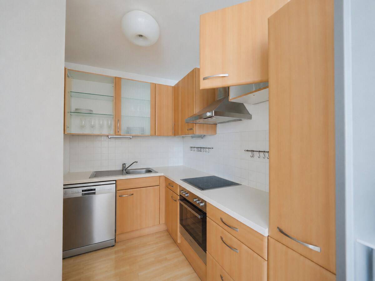 Kleine, funktionale Einbauküche mit Holzfronten, modernen Geräten und Fliesenrückwand.