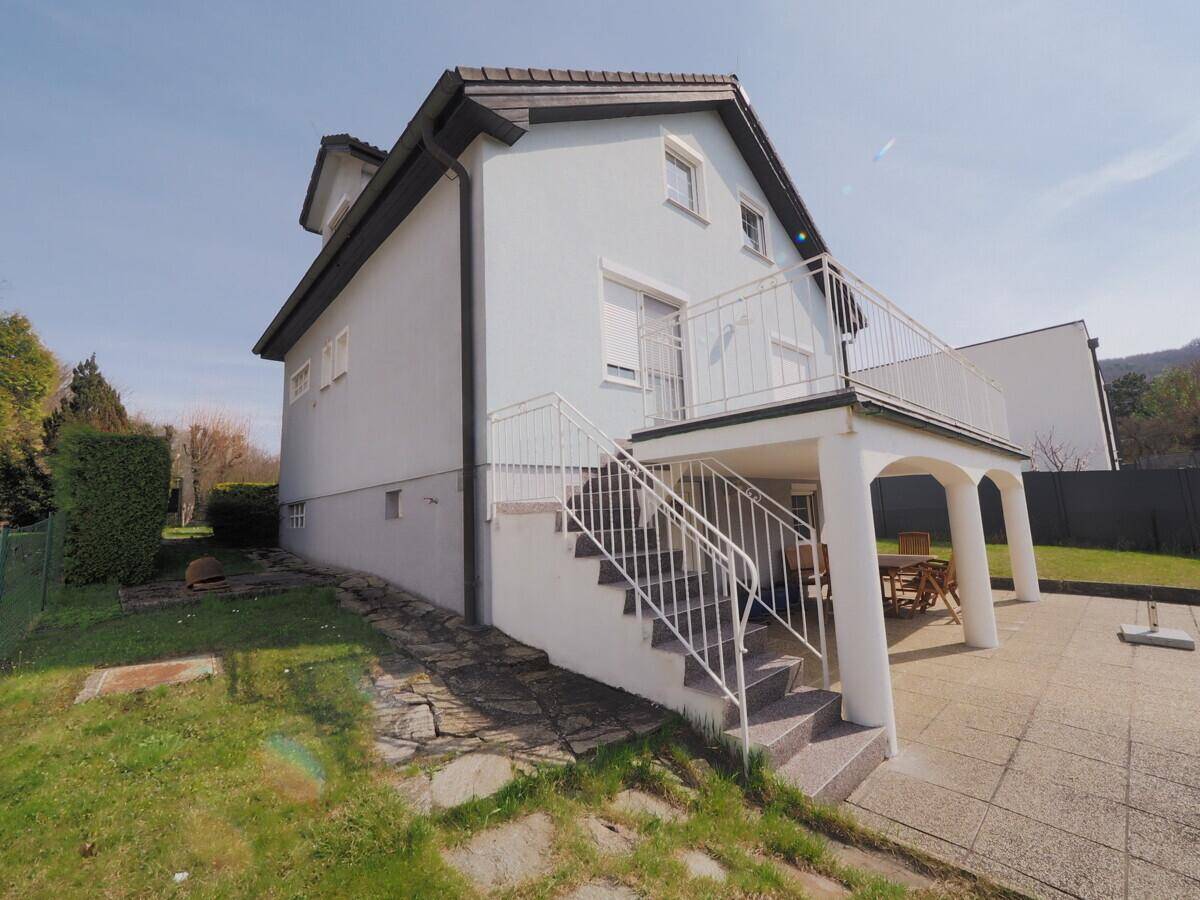 Seitenansicht des Hauses mit Außentreppe zum Balkon und gepflasterter Terrasse.