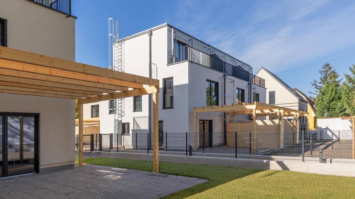 Seitenansicht eines modernen Reihenhauses mit Balkonen, Terrasse und Holzpergola im Gartenbereich.