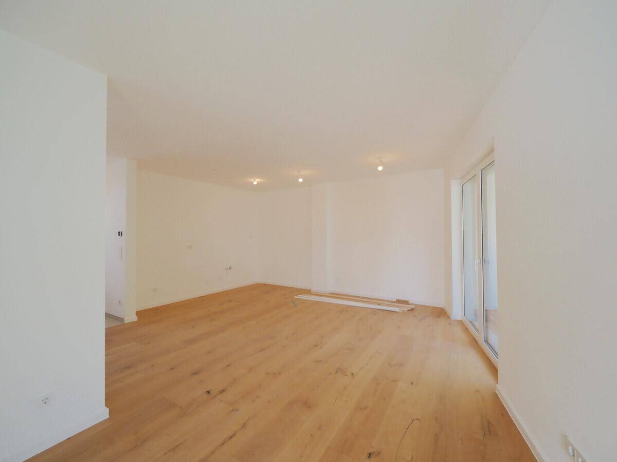 Lichtdurchflutetes Wohnzimmer mit hellem Holzfußboden und großen Fenstern.