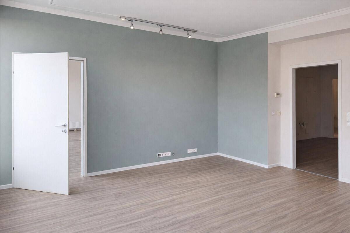 Heller Büroraum mit einer dezenten graugrünen Wandfarbe und modernem Laminatboden.