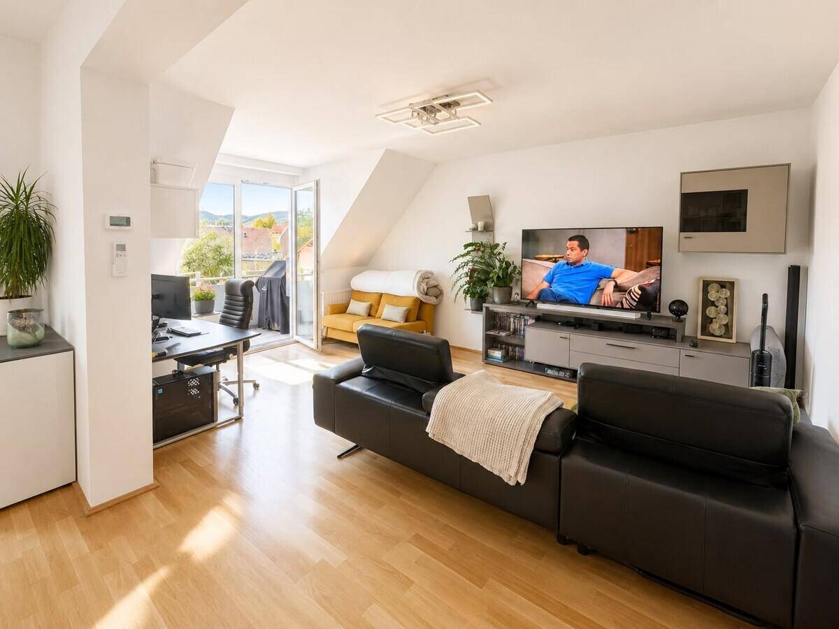 Geräumiges Wohnzimmer mit großem Fernseher, Arbeitsbereich und direktem Zugang zum Balkon.