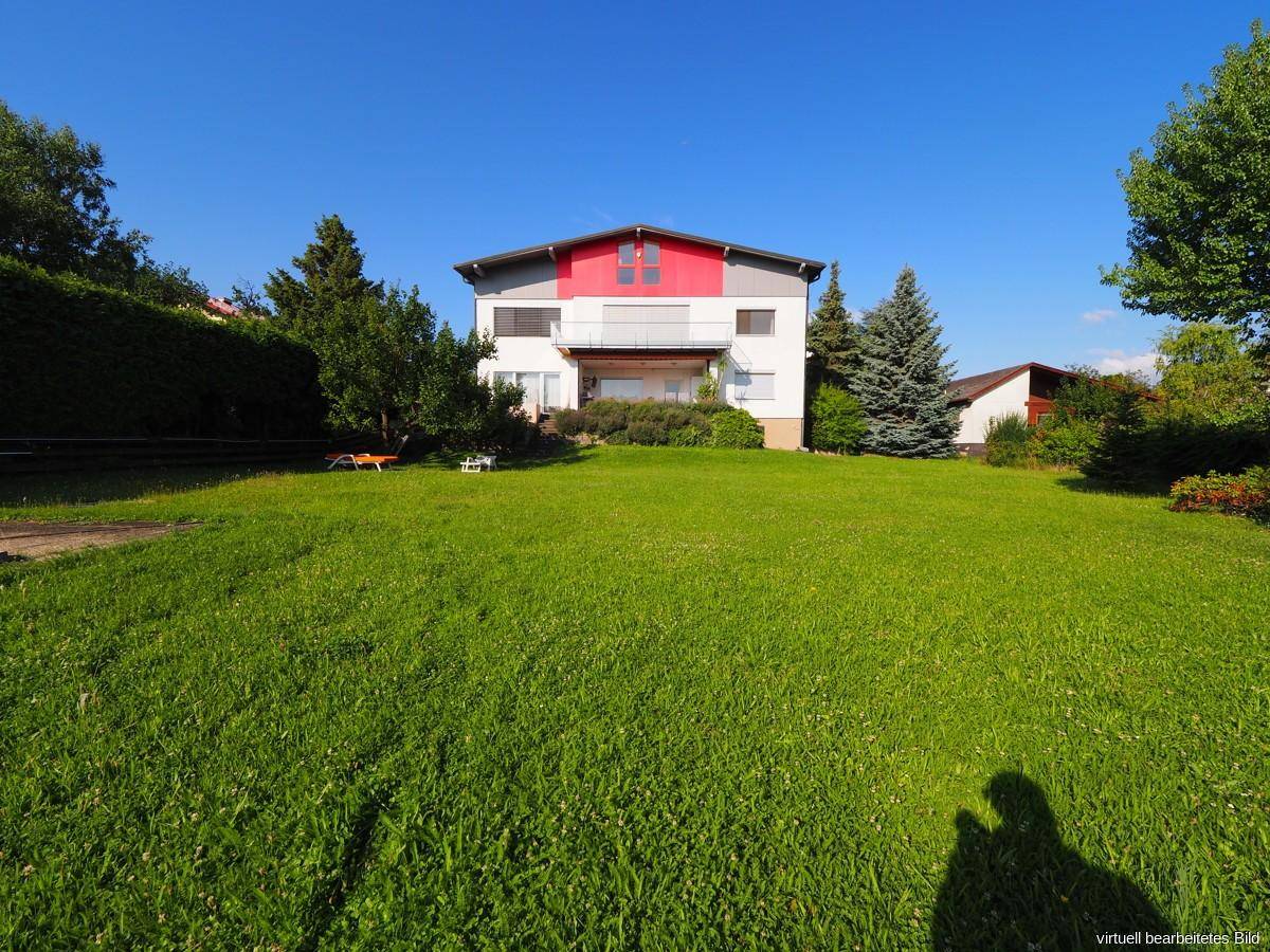 Vorderansicht des Hauses mit gepflegtem Rasen und Bäumen unter blauem Himmel.