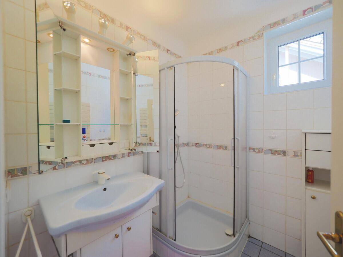 Helles Badezimmer mit Duschkabine, Waschbecken und weiß gefliesten Wänden.