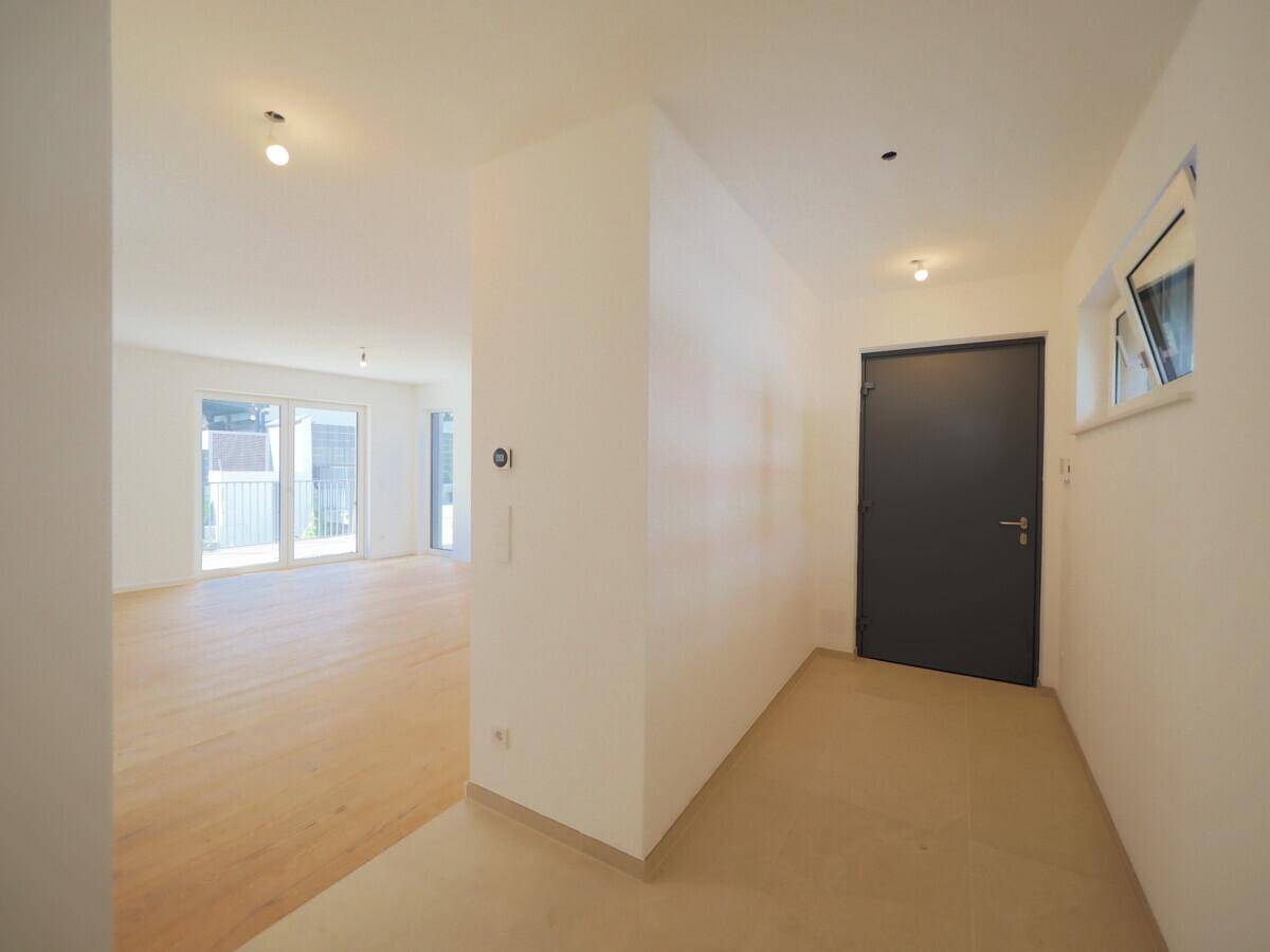 Heller Eingangsbereich mit Holzboden, weiß gestrichenen Wänden und einer modernen dunklen Eingangstür.