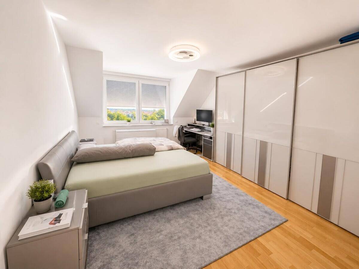 Helles Schlafzimmer mit großem Bett, Einbauschränken und einem Arbeitsplatz am Fenster.
